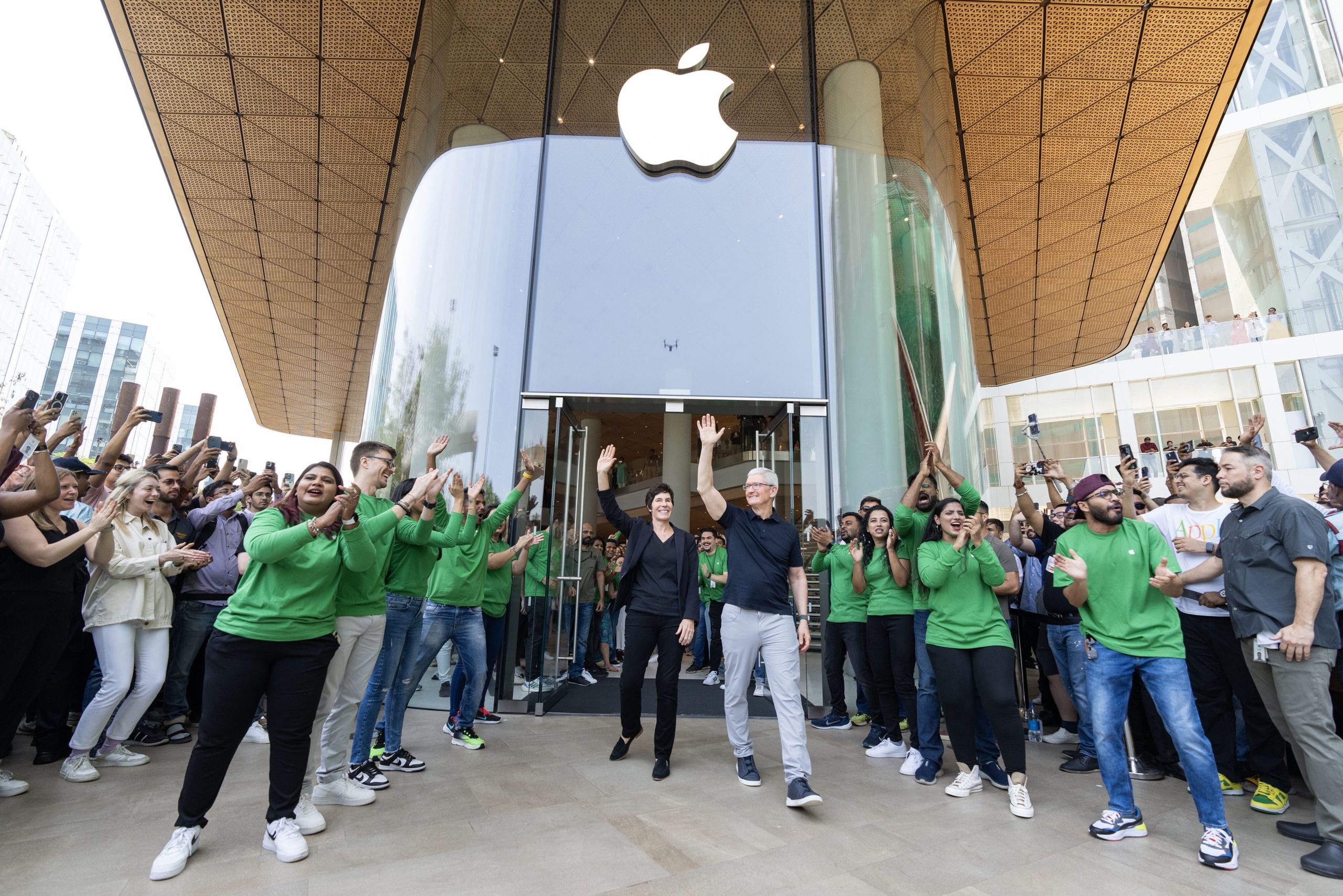 Tim and Deirdre stand and wave in front of the open doors at Apple BKC, surrounded by team members and customers.